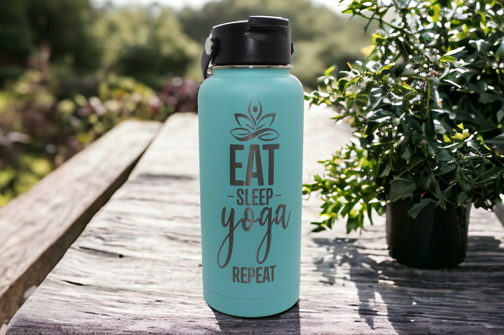 "Image of a teal-colored 32 oz. RTIC water bottle featuring laser-engraved 'Eat, Sleep, Yoga, Repeat'. The laser engraving adds a motivational touch, making it an ideal gift for yoga enthusiasts or anyone striving for balance and wellness. Additionally, the bottle can be further personalized to add a unique and thoughtful touch."