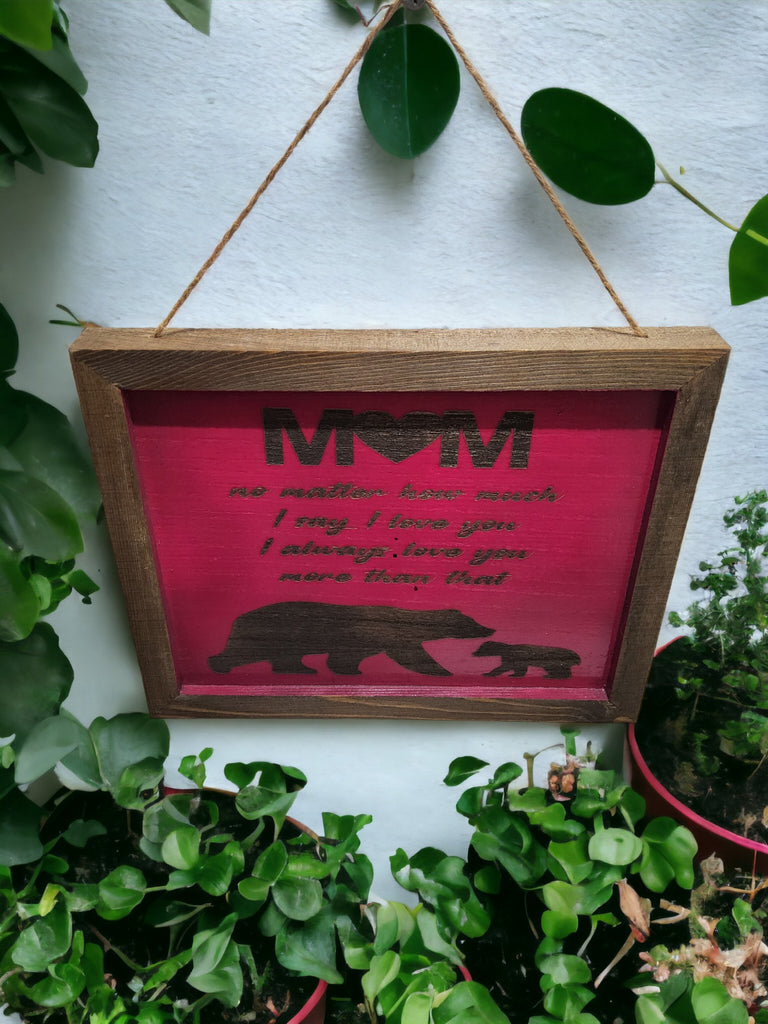 A rustic wooden sign with laser-engraved text that reads "Mom, no matter how much I say I love you, I always love you more than that." evoking warmth and sentimentality."